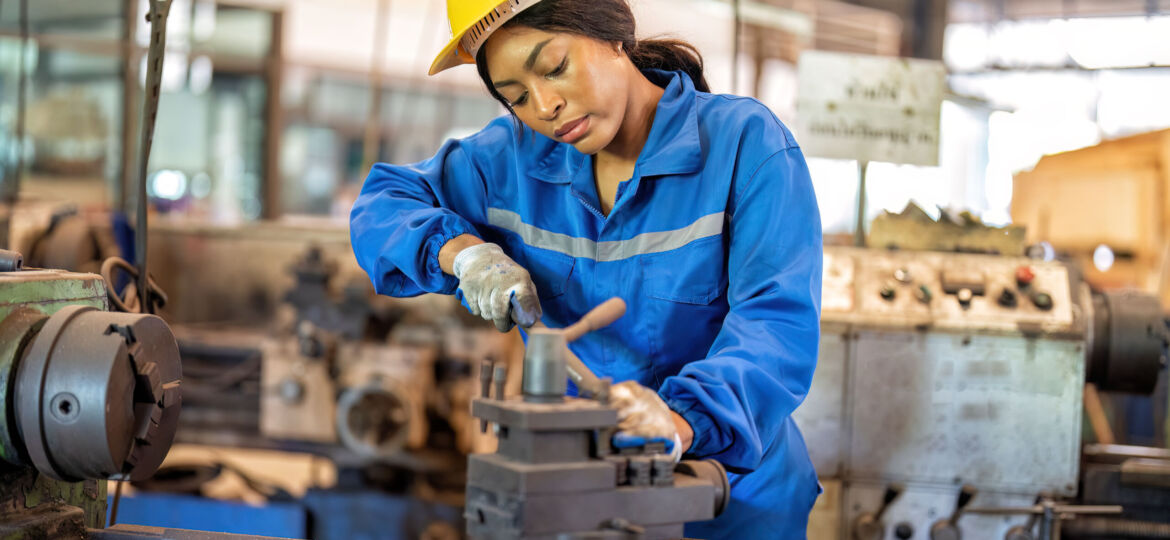 Woman worker in uniform operating machine at factory concentrate on fabrication job on lathe